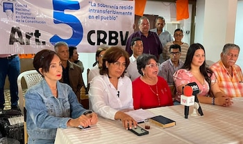 Grupo de personas en una reunión sentadas y de pie. Un cartel blanco dice "Comité Nacional Promotor en Defensa de la Constitución, Art. 5 CRBV". Un micrófono