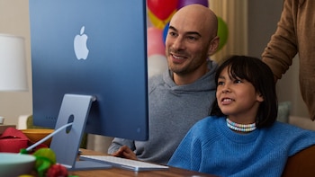 Un hombre y una niña están sentados frente a una computadora iMac azul de Apple sobre una mesa de madera