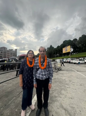 Un hombre y una mujer están de pie al aire libre con guirnaldas de flores naranjas alrededor del cuello