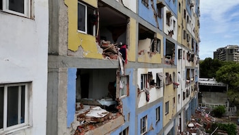 Edificio de varios pisos con daños estructurales y fachadas colapsadas, mostrando escombros, ventanas rotas y ropa. Cielo nublado