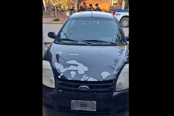 Un coche Ford Ka negro con pintura descascarada en el capó. Al fondo, se ven agentes policiales y una patrulla blanca con el número 0911