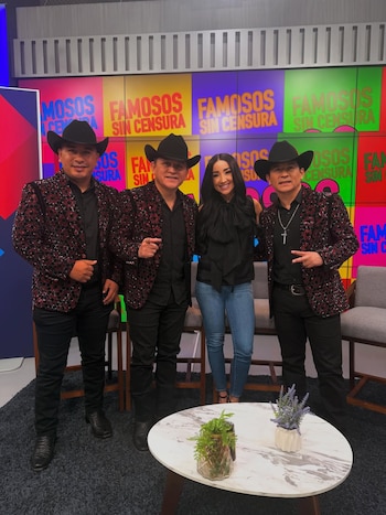 Cuatro personas, tres hombres y una mujer, de pie en estudio. Sombreros vaqueros, chaquetas lentejuelas, blusa negra, jeans. Muro "Famosos Sin Censura", mesa con plantas