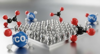 Superficie metálica pulida con hileras de esferas plateadas pequeñas y una grande central, rodeada de modelos moleculares de CO₂ (rojo/negro/rojo y azul) y H₂ (azul/blanco).