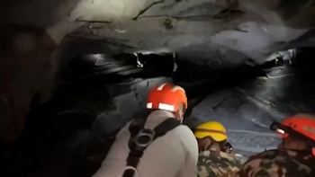 Tres personas con cascos de seguridad e indumentaria táctica se desplazan por el interior de una cueva oscura y estrecha