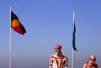 Artistas aborígenes australianos vestidos tradicionalmente junto a una bandera aborigen y otra bandera de los isleños del estrecho de Torres en la playa Coogee de Sídney. REUTERS/David Gray/Archivo