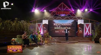 Un presentador de pie y tres mujeres sentadas en un sofá verde en el set de televisión de 'La Granja VIP', con un gran monitor mostrando el nuevo horario y luces moradas