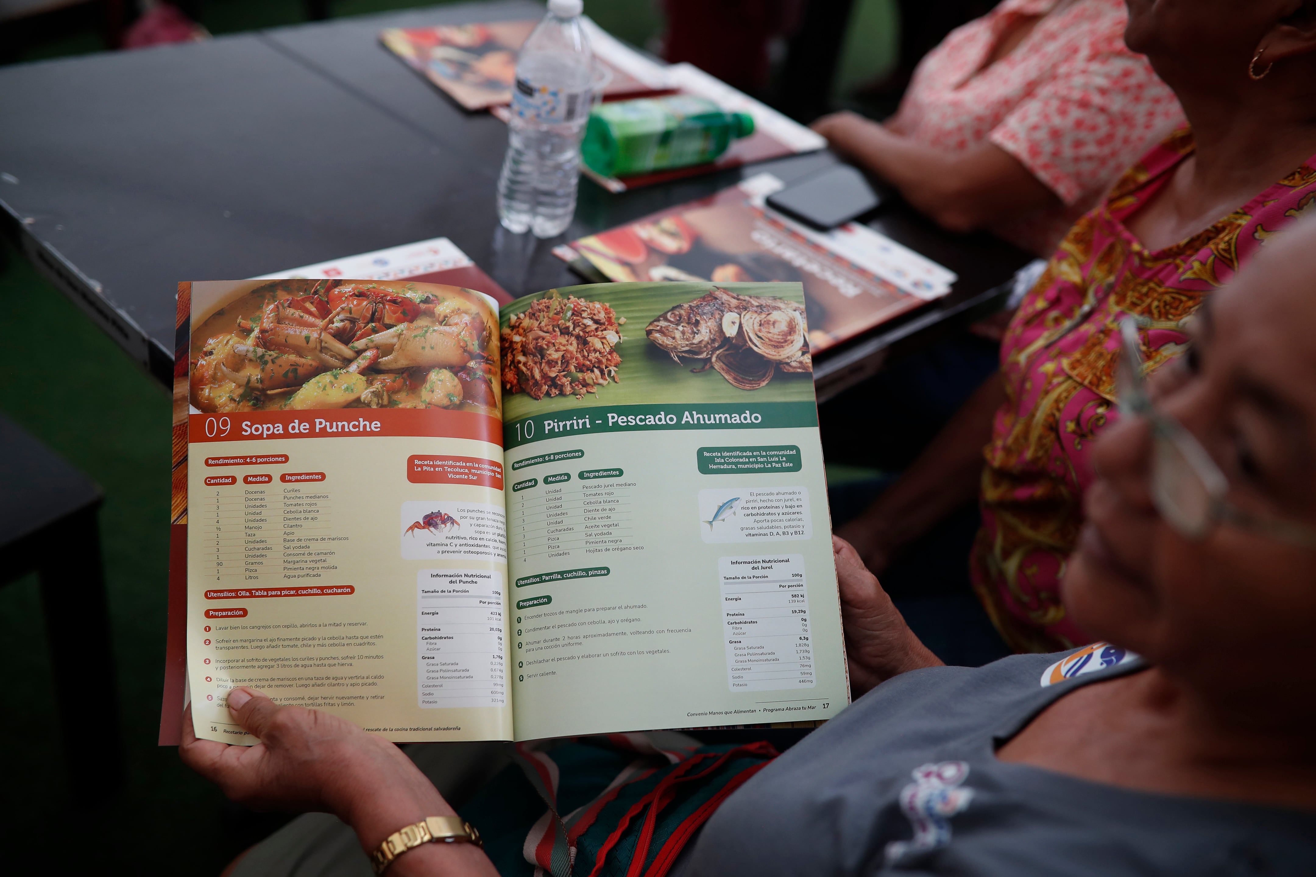 Una mujer sonríe mientras sirve platos de comida, representando la iniciativa Manos que Alimentan, financiada por Cooperación Española y liderada por Asamblea de Cooperación por la Paz, en un evento en San Salvador. (Agencia EFE)