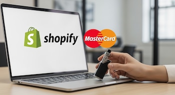 Laptop abierta con logos de Shopify y Mastercard en pantalla, mano sostiene un vape metálico sobre el teclado en un escritorio de madera.