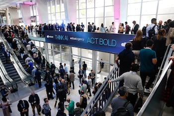 Una multitud camina por un vestíbulo con escaleras mecánicas debajo de un cartel azul que dice THINK AI ACT BOLD
