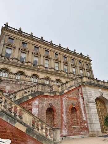 Fachada de un edificio histórico de piedra y ladrillo con una amplia escalinata exterior que presenta balaustradas y arcos