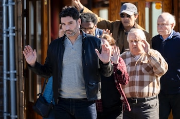 Un hombre con chaqueta de cuero y barba, Colin Glass, y varias personas más levantan las manos en el aire frente a un edificio con una puerta de madera