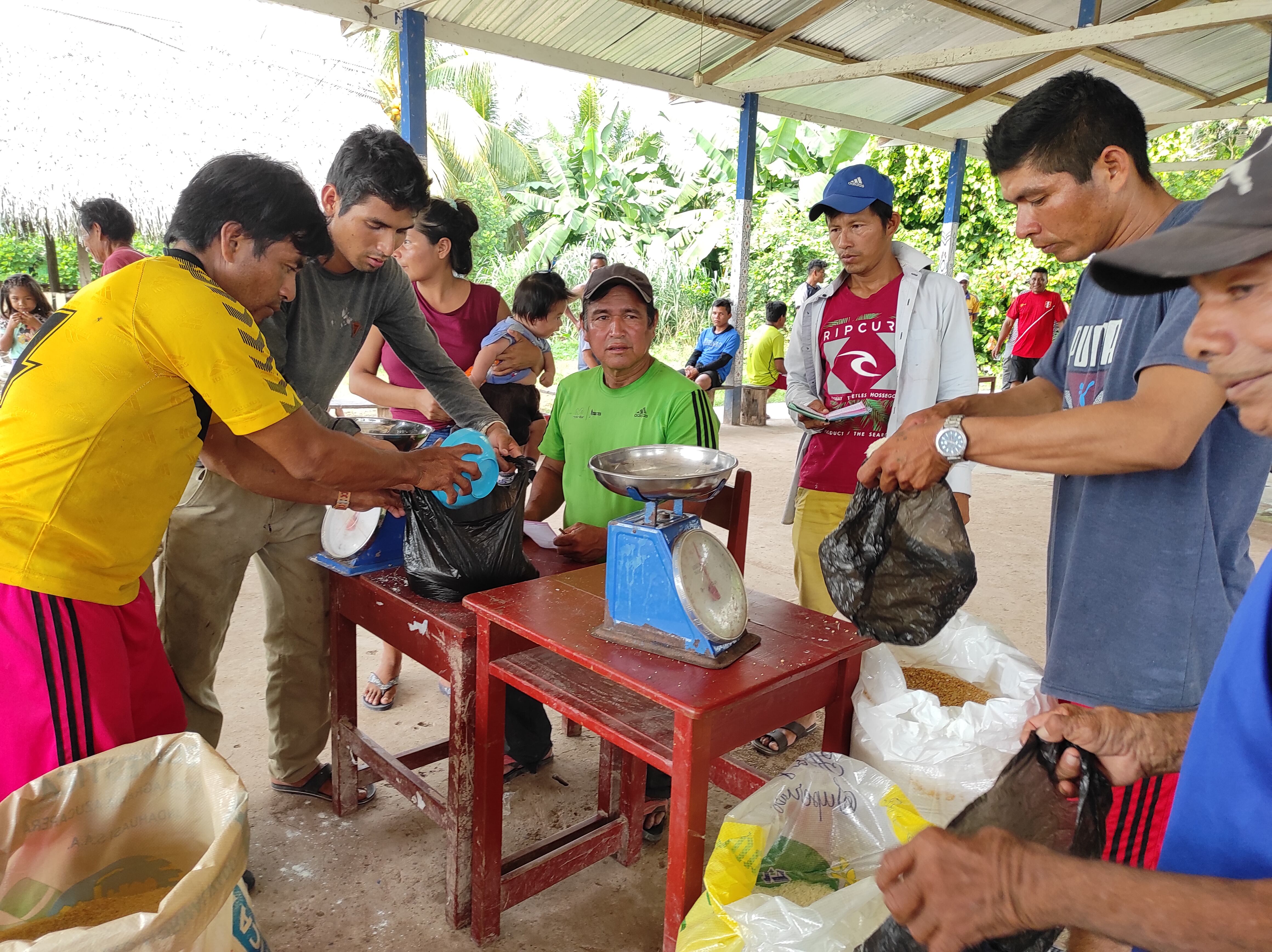 Miembros de la comunidad shipibo-konibo en Ucayali pesan productos agrícolas con básculas bajo un cobertizo de techo metálico.