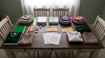 Mesa de madera con mochilas, cuadernos, lápices, reglas, uniformes escolares doblados, sobres con dinero y documentos del Gobierno de México.