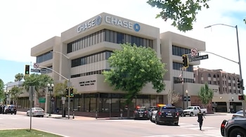 Vista exterior de un edificio Chase en una esquina de calle con múltiples vehículos policiales, luces encendidas y un oficial en la calle