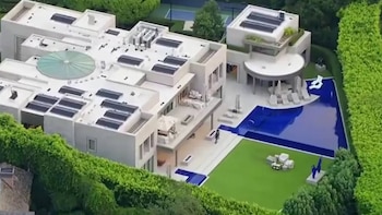 Vista aérea de una residencia blanca con paneles solares, una piscina azul y un jardín rodeado por setos verdes