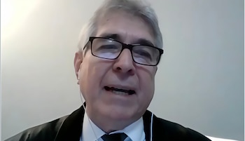 Hombre canoso con gafas, traje, corbata, auriculares con cable y boca abierta sobre fondo claro