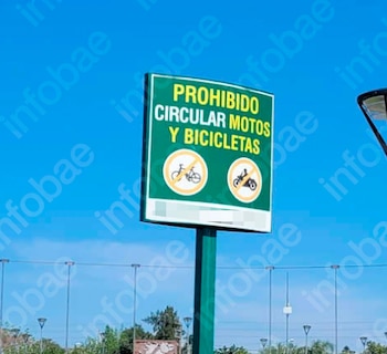 Un cartel verde de prohibición con texto amarillo que indica 'PROHIBIDO CIRCULAR MOTOS Y BICICLETAS', y dos símbolos de prohibición para bicicleta y motocicleta