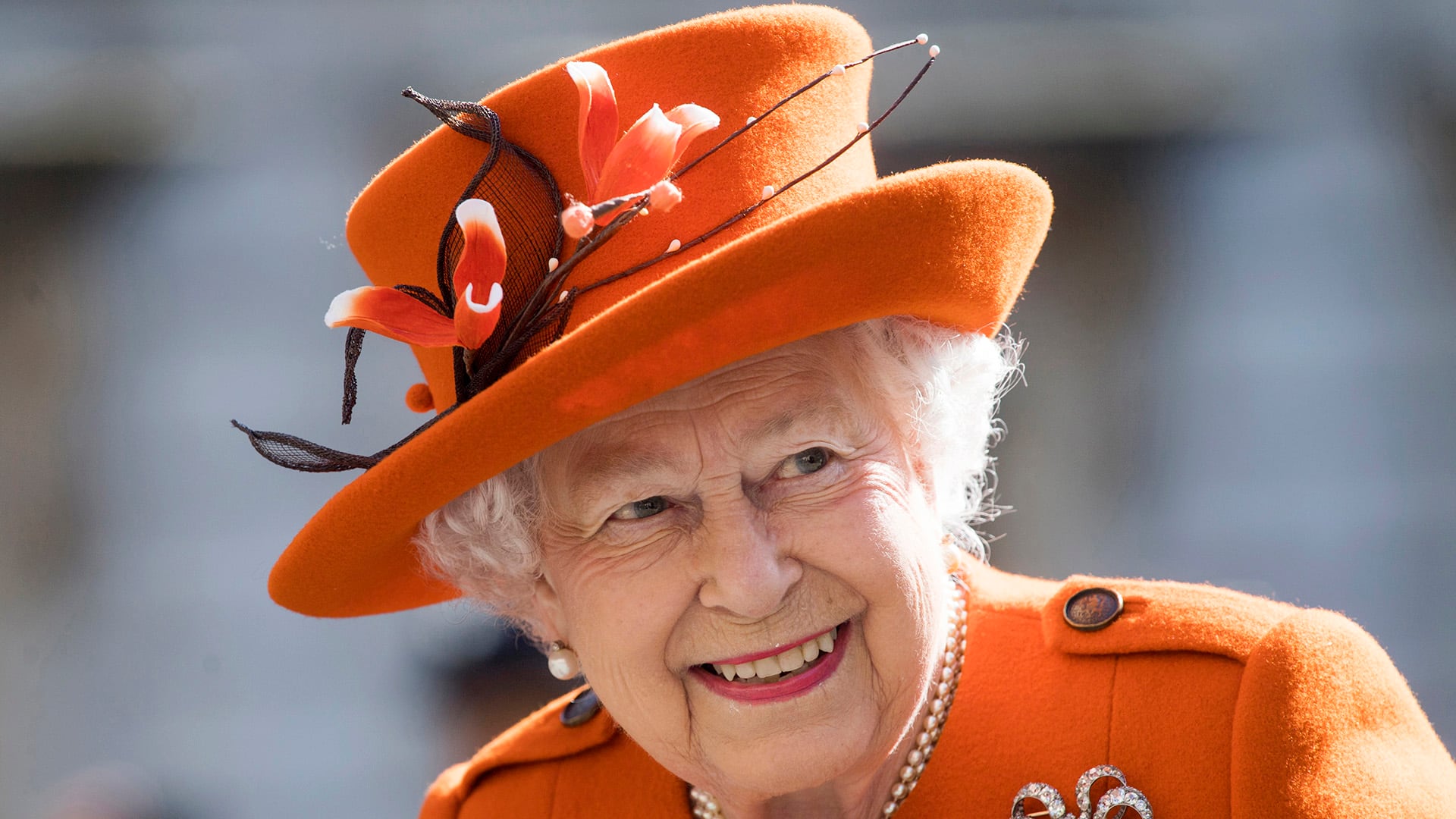 Look en naranja intenso, con sombrero decorado con flores y ramas marrones, equilibrado por perlas y broche en espiral con cristales (EFE)