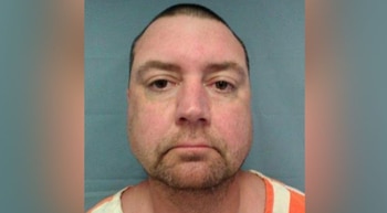 Primer plano de un hombre caucásico de mediana edad, con barba incipiente, frente a un fondo azul claro. Viste una camisa a rayas naranjas y blancas