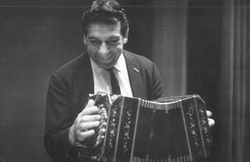 Fotografía en blanco y negro de un hombre vestido con traje y corbata que sostiene y toca un acordeón de botones