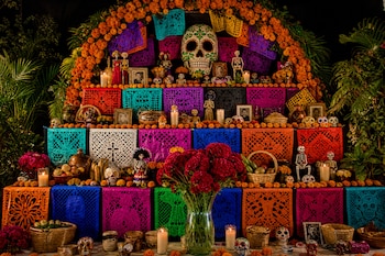 Altar de niveles con papel picado colorido, arco de flores de cempasúchil, calaveras artesanales, velas, retratos y canastos con frutas.