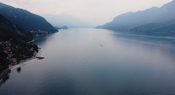 Vista aérea de un gran lago azulado con montañas a cada lado, un pueblo costero, una playa con carretera y dos barcos en la superficie