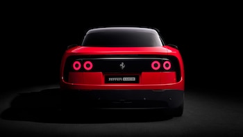 Vista trasera de un Ferrari Luce rojo, un vehículo 100% eléctrico, con luces traseras circulares encendidas y el logo Ferrari en la parte central sobre fondo negro