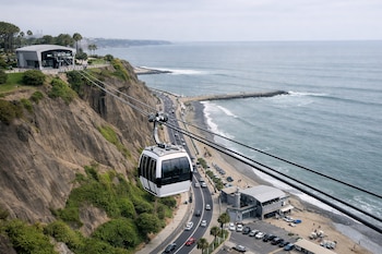 Teleférico Vaivén Miraflores con cabina blanca, dos estaciones modernas, acantilado costero, playa, mar Pacífico, carretera, malecón y zonas verdes.