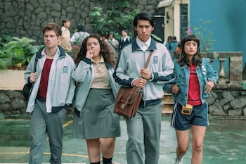 Cuatro jóvenes, dos hombres y dos mujeres, caminan por una cancha. Dos hombres y una mujer visten chaqueta gris con escudo; otra mujer lleva chaqueta vaquera y shorts