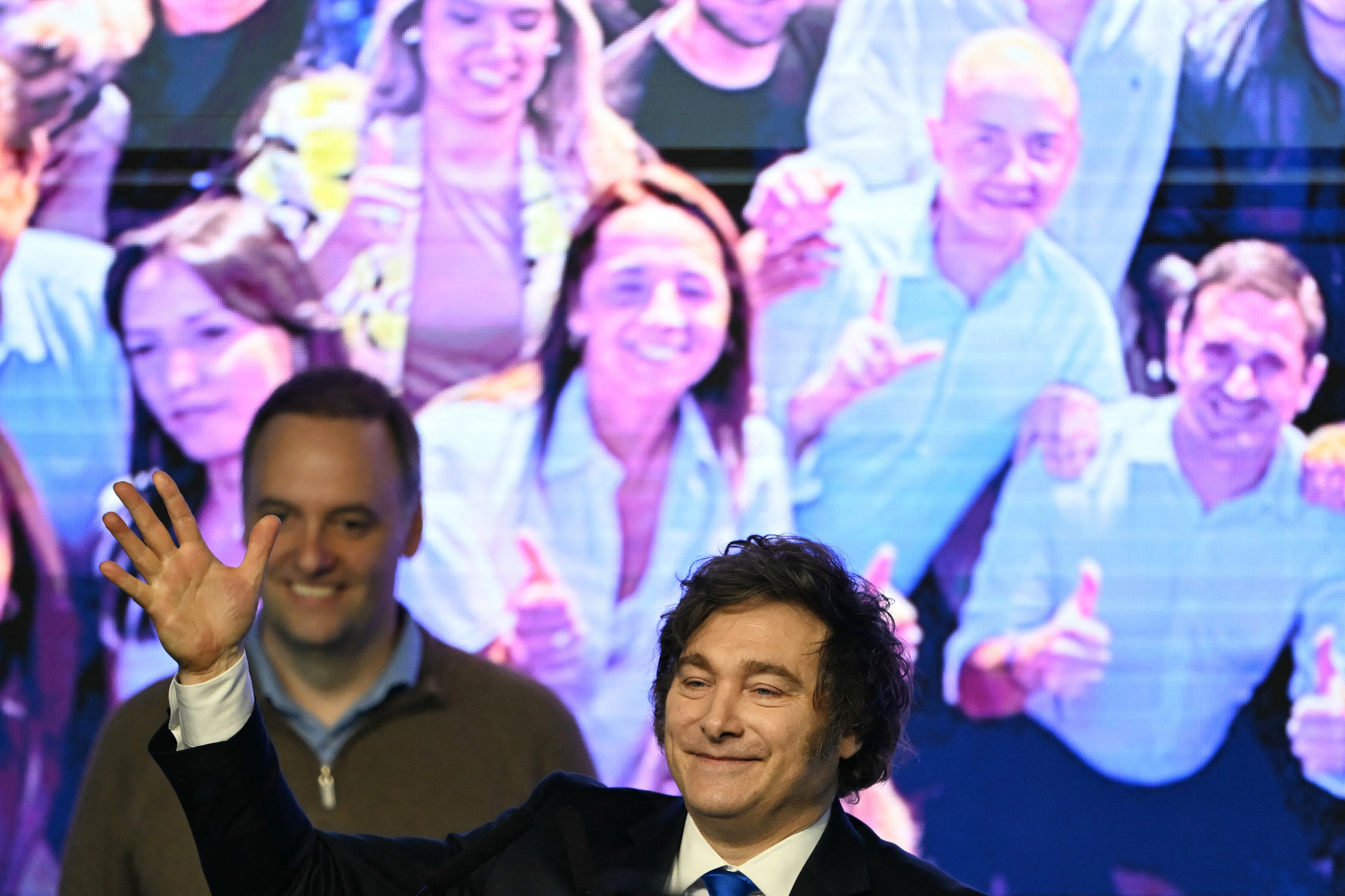Argentina's President Javier Milei waves to supporters next to the spokesperson for the Presidency Manuel Adorni at the ruling party's La Libertad Avanza headquarters following the results of the national midterm legislative election in Buenos Aires on October 26, 2025. Argentina's budget-slashing leader Javier Milei pulled off a stunning win in Sunday's midterm elections, boosting the flagging reform agenda of the US-backed right-winger. (Photo by Luis ROBAYO / AFP)