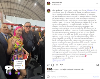 Una mujer con cabello rosa y vestido multicolor sonríe y saluda, de pie junto a un hombre con gafas de sol oscuras y traje en un evento concurrido