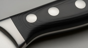 Primer plano del mango de un cuchillo negro texturizado que tiene tres remaches circulares plateados y una parte metálica lisa en un extremo.