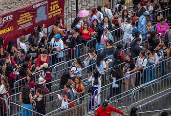 Multitud de personas avanzando a través de pasillos delimitados por vallas metálicas en un espacio al aire libre
