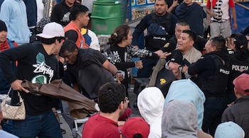 Varias personas forcejean y discuten en una calle mientras dos agentes de policía con chalecos negros intervienen.