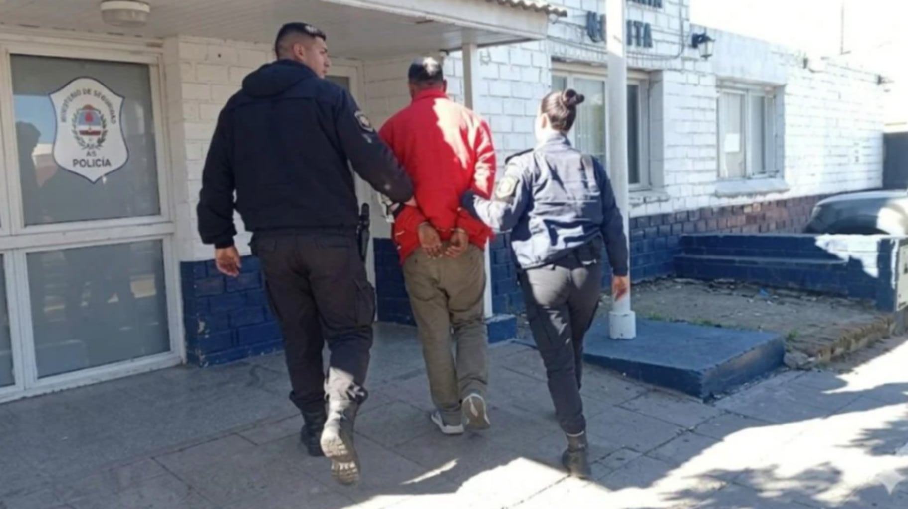 Dos agentes de policía escoltan a un hombre esposado en Mar del Plata, detenido bajo cargos de violencia doméstica (La Capital de Mar del Plata)