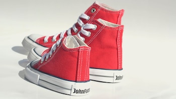 Primer plano de dos zapatillas de lona rojas John Foos, una grande y otra pequeña, con cordones y suelas blancas, sobre un fondo claro