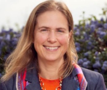 Retrato de una mujer de mediana edad con cabello rubio largo y suelto, vistiendo un blazer azul y una blusa naranja, sonriendo ligeramente