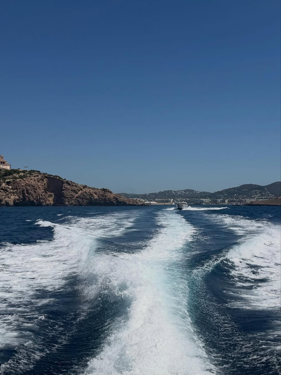 La costa rocosa de Ibiza desde el agua, con otra embarcación visible en el horizonte