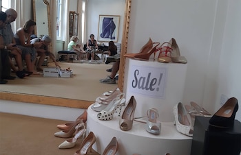 Zapatos de tacón sobre un expositor con un cartel de oferta y varias personas sentadas que se prueban calzado frente a un espejo