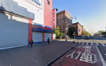 Fachada de un comercio con persianas metálicas cerradas, un cartel vertical rojo y un cruce peatonal en una esquina urbana