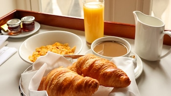Un desayuno con zumo, café, cereales y croisants (Canva)