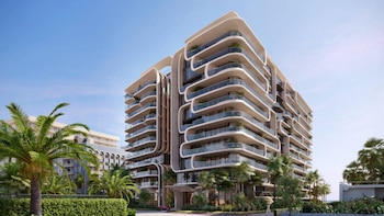 Edificio moderno de gran altura con múltiples balcones curvos de cristal y líneas onduladas, rodeado de palmeras y vegetación bajo un cielo azul claro