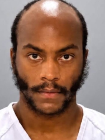 Fotografía policial de Eric Lewis, un hombre de tez morena con barba, bigote y calvicie parcial, vestido con una camiseta blanca