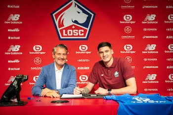 Orlando Gill y un directivo sentados ante un escritorio rojo firmando un documento, frente a un panel con el escudo del LOSC Lille