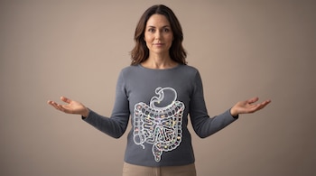 Una mujer vestida con un suéter gris sostiene las manos abiertas junto a un esquema del sistema digestivo con luces en su torso.