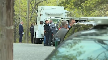Agentes de policía y civiles se congregan cerca de vehículos policiales y un camión de emergencia en una calle arbolada de Long Island