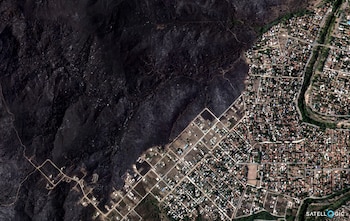 Imagen aérea satelital mostrando un paisaje dividido. A la izquierda, terreno oscuro y quemado. A la derecha, una zona residencial con casas, calles y vegetación