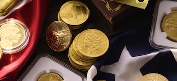 Monedas de oro de colección, sueltas y en estuches protectores de plástico, dispuestas junto a una bandera de Estados Unidos