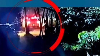 Imagen nocturna enmarcada en un círculo rojo que señala un vehículo con luces encendidas en un camino junto a la vegetación