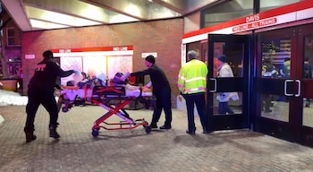 Paramédicos empujan una camilla con una persona cubierta hacia la entrada de la estación de metro Davis Red Line, con nieve a la izquierda